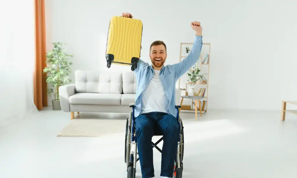 man in wheelchair holding suitcase in a hotel room